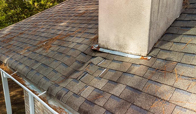 A damaged roof with missing and lifted shingles